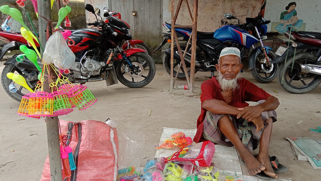 কিশোরগঞ্জ উপজেলা স্বাস্থ্য কমপ্লেক্সের পাশে খেলনার পসরা সাজিয়ে বসে আছেন মজিদ উদ্দিন। ছবি : কালবেলা