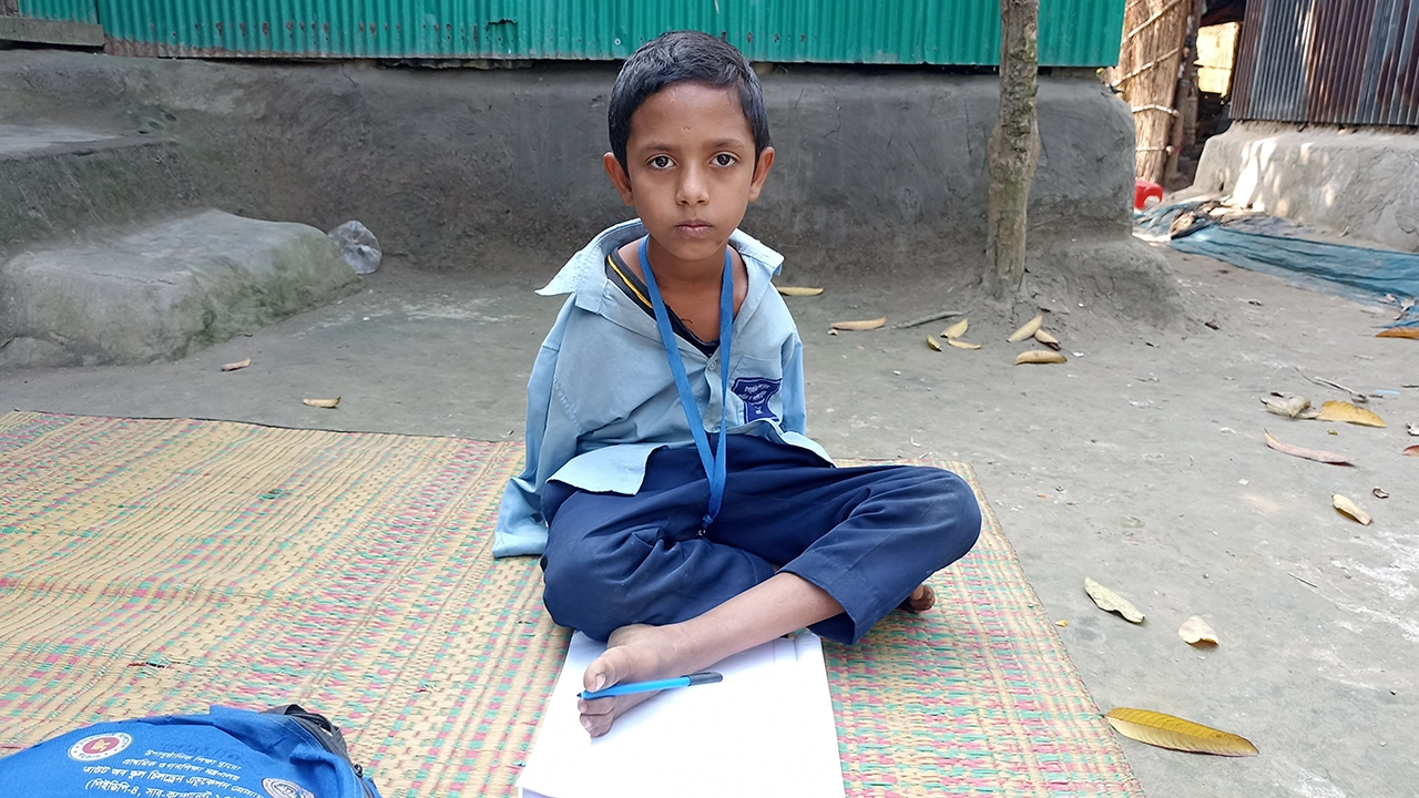 হাত না থাকায় পা দিয়ে লেখে আসাদুল। ছবি : কালবেলা