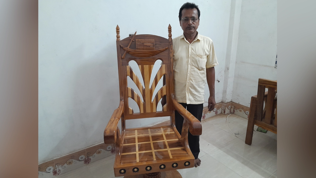 প্রধানমন্ত্রীকে উপহার প্রদানের আঁকুতি নিয়ে চেয়ারের পাশে দাঁড়ানো কাঠমিস্ত্রি হীরেন্দ্র চন্দ্র সরকার (হিরু)। ছবি : কালবেলা