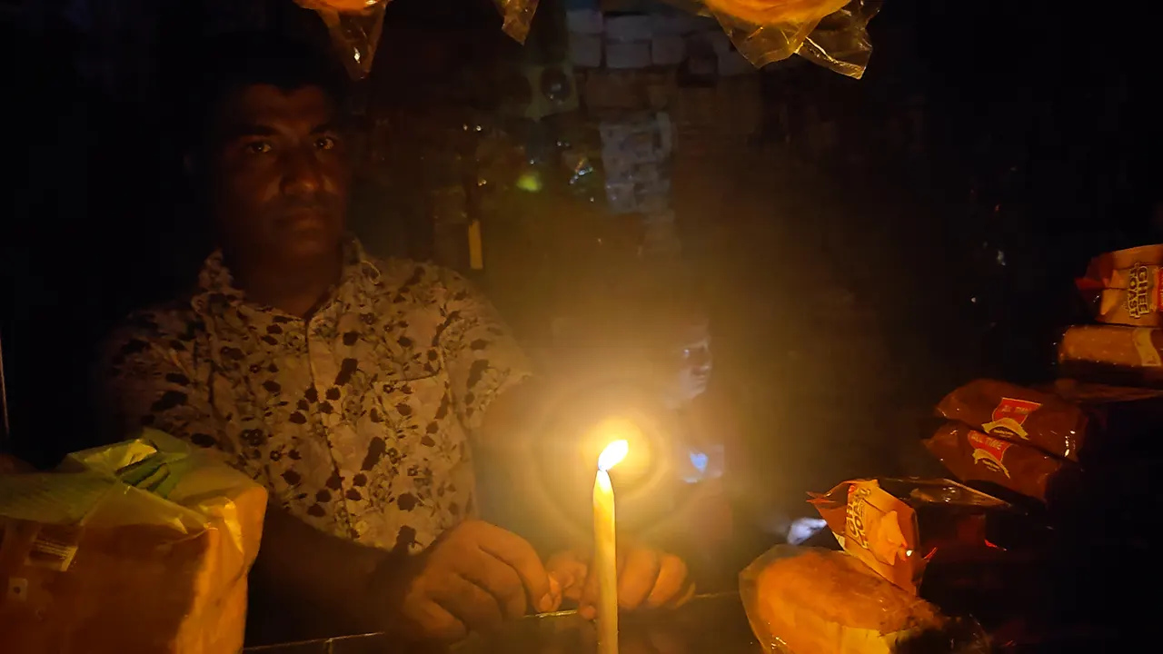 মোমবাতি জ্বালিয়ে কাজ করছেন আখাউড়ার দোকানিরা। ছবি : কালবেলা