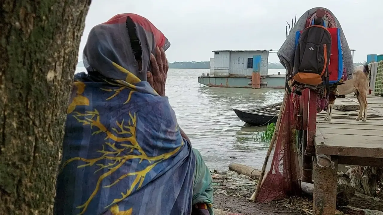রিমালে ক্ষতিগ্রস্ত ফিরোজা বেগম গালে হাত দিয়ে বসে আছেন নদী তীরে । ছবি : কালবেলা